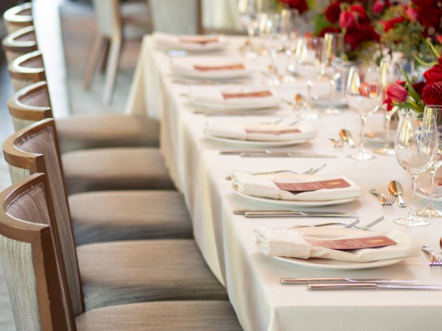 A formal dining table set with white napkins, elegant glassware, and vibrant red floral centerpieces for a special event or celebration.