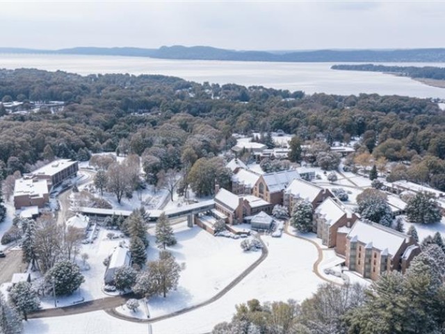 A snowy town scene with buildings, trees, and a river in the background, all covered in snow, creating a wintery landscape and serene atmosphere.