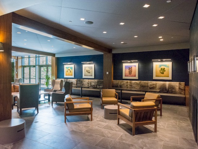 Picture shows lobby area for River Fox Restaurant and bar, a modern lounge with comfortable seating areas. There is modern artwork on the walls, a large fireplace is shown on the right, giving a cozy atmosphere.