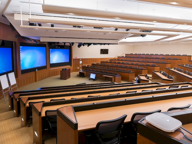 This image shows The Pit Windrose's famous large lecture hall, with tiered seating and three large screens.