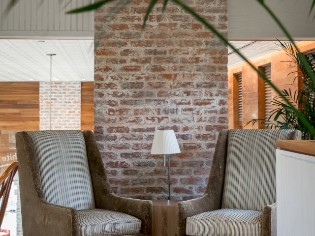 The image shows a cozy sitting area with two upholstered chairs facing each other, a small table with a lamp between them, and a brick wall in the background. This is located inside Cafe 56 on the second floor.