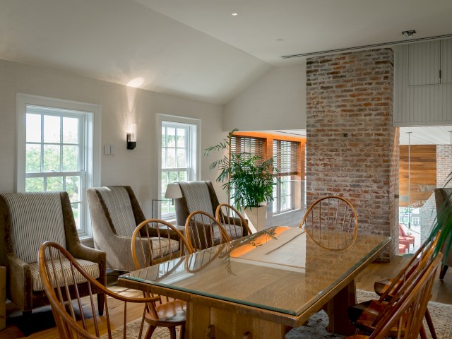 The image shows a well-lit cottage style meeting space with a large wooden table and chairs, with a brick accented wall located inside Cafe 56 on the second floor.