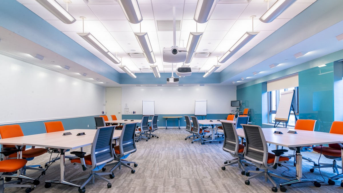 A modern conference room with U-shaped tables, ergonomic chairs, whiteboards, and ceiling-mounted projectors, featuring bright lighting.