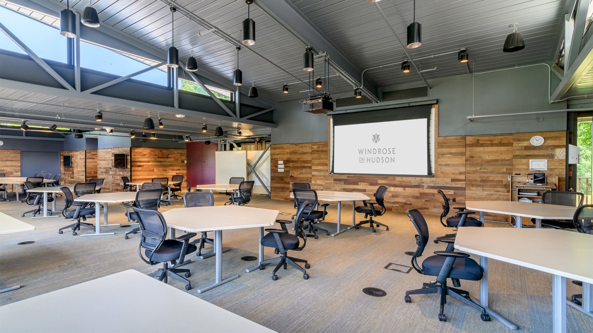 This image shows a modern, open office space with numerous desks and chairs. There's a projector screen displaying 