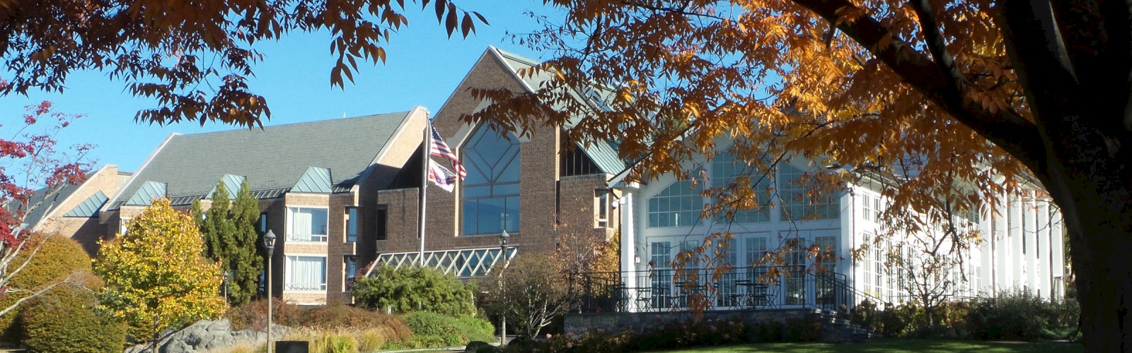 A large building complex with modern architectural elements is surrounded by lush green lawn and autumn trees under a clear blue sky.