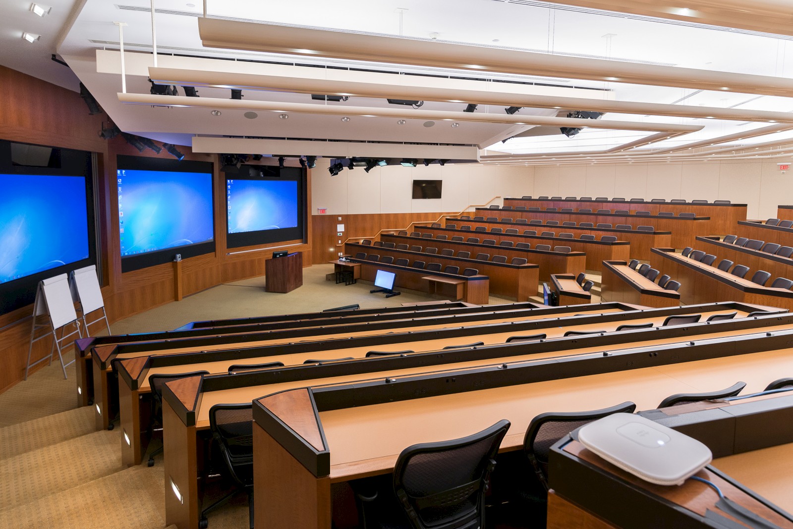 A modern lecture hall with tiered seating, multiple screens, and a podium, designed for presentations and lectures.