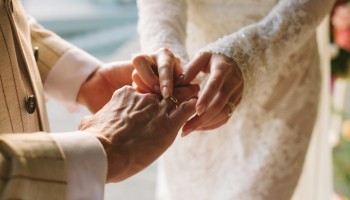 A person is placing a ring on another's finger, possibly during a wedding ceremony.
