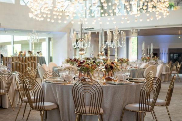 Elegant event setup with decorative tables, flowers, and unique chairs under ornate lighting.