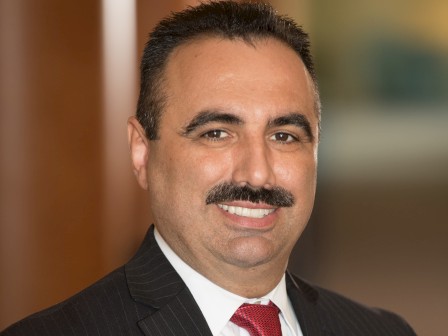 A person is smiling, wearing a pinstripe suit and red tie, and posing indoors.