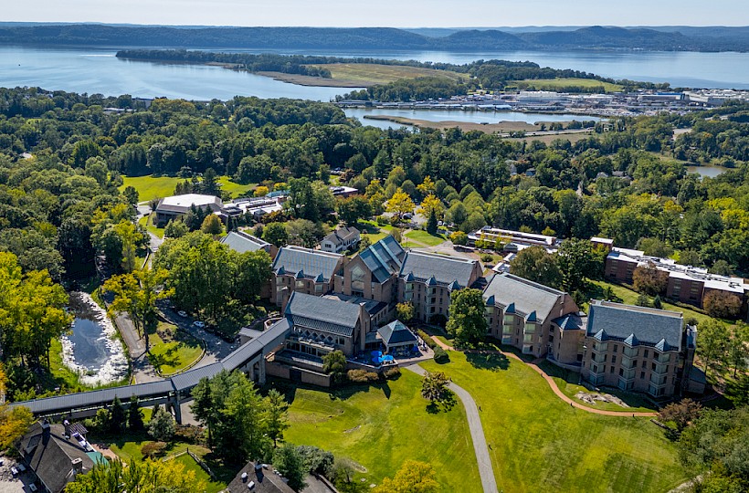 An aerial view of a large building complex surrounded by lush greenery, with a lake and distant landscape in the background.