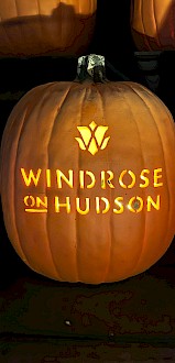 A carved pumpkin with the words “WINDSROSE ON HUDSON” lit from inside, glowing orange on dark display.