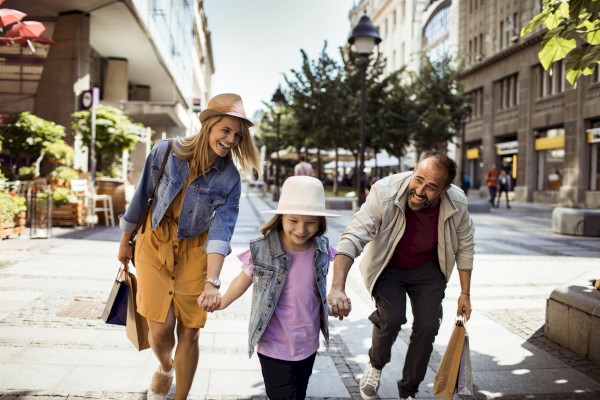 parents and daughter holding hands while walking down the city with shopping bags