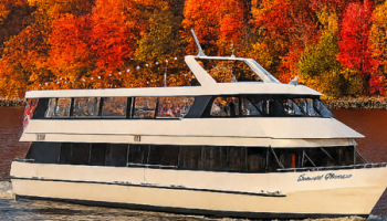 A white boat cruising on a river, surrounded by vibrant autumn-colored trees in the background.