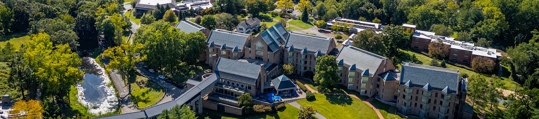 This image shows an aerial view of a large estate with several buildings, surrounded by trees and near a body of water.