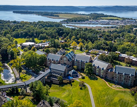 This image shows an aerial view of a large estate with several buildings, surrounded by trees and near a body of water.