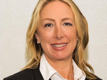 The image shows a person wearing a black blazer and white shirt, smiling against a plain background.