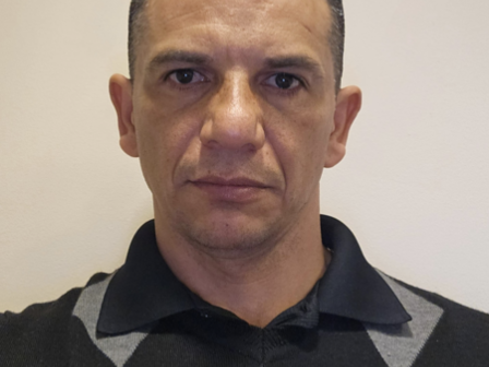 A person wearing a patterned sweater and a name tag is looking directly at the camera.