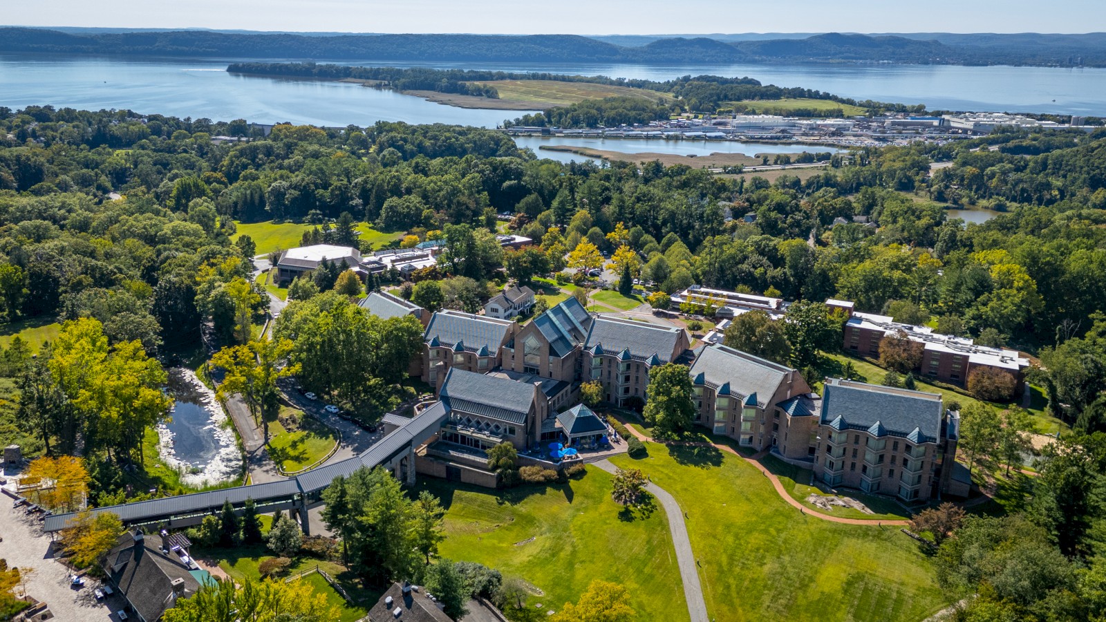 An aerial view of a large estate surrounded by lush greenery, with a body of water in the background under a clear sky.