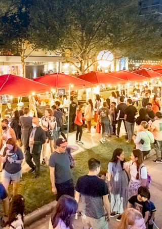 A bustling night market with red tents and string lights, filled with people browsing and enjoying the lively atmosphere.