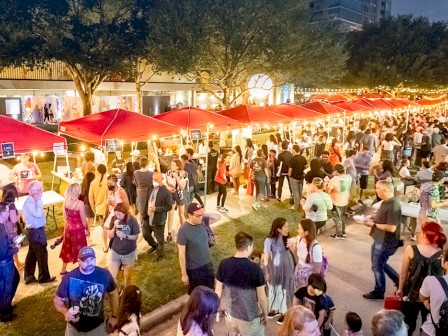 A bustling night market with red tents and string lights, filled with people browsing and enjoying the lively atmosphere.