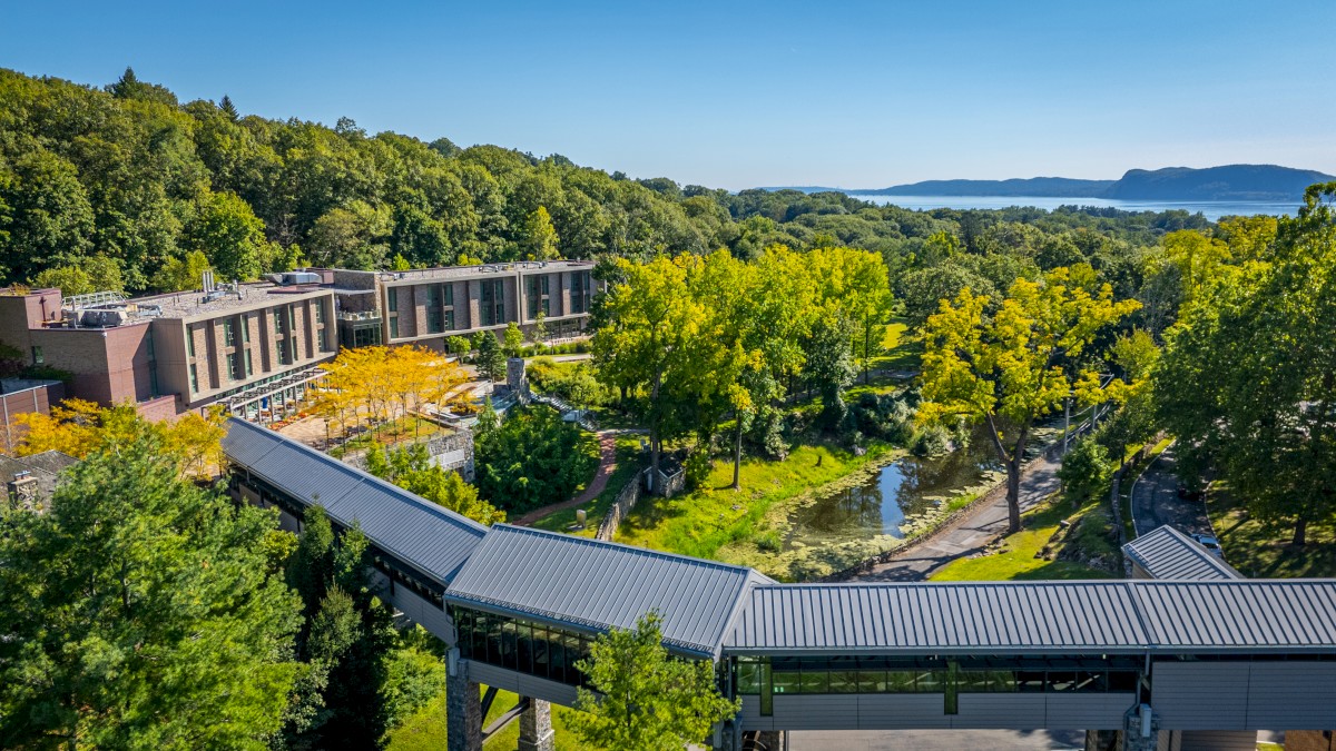 A scenic view features modern buildings amid lush greenery and a winding pathway, with distant hills and water in the background.