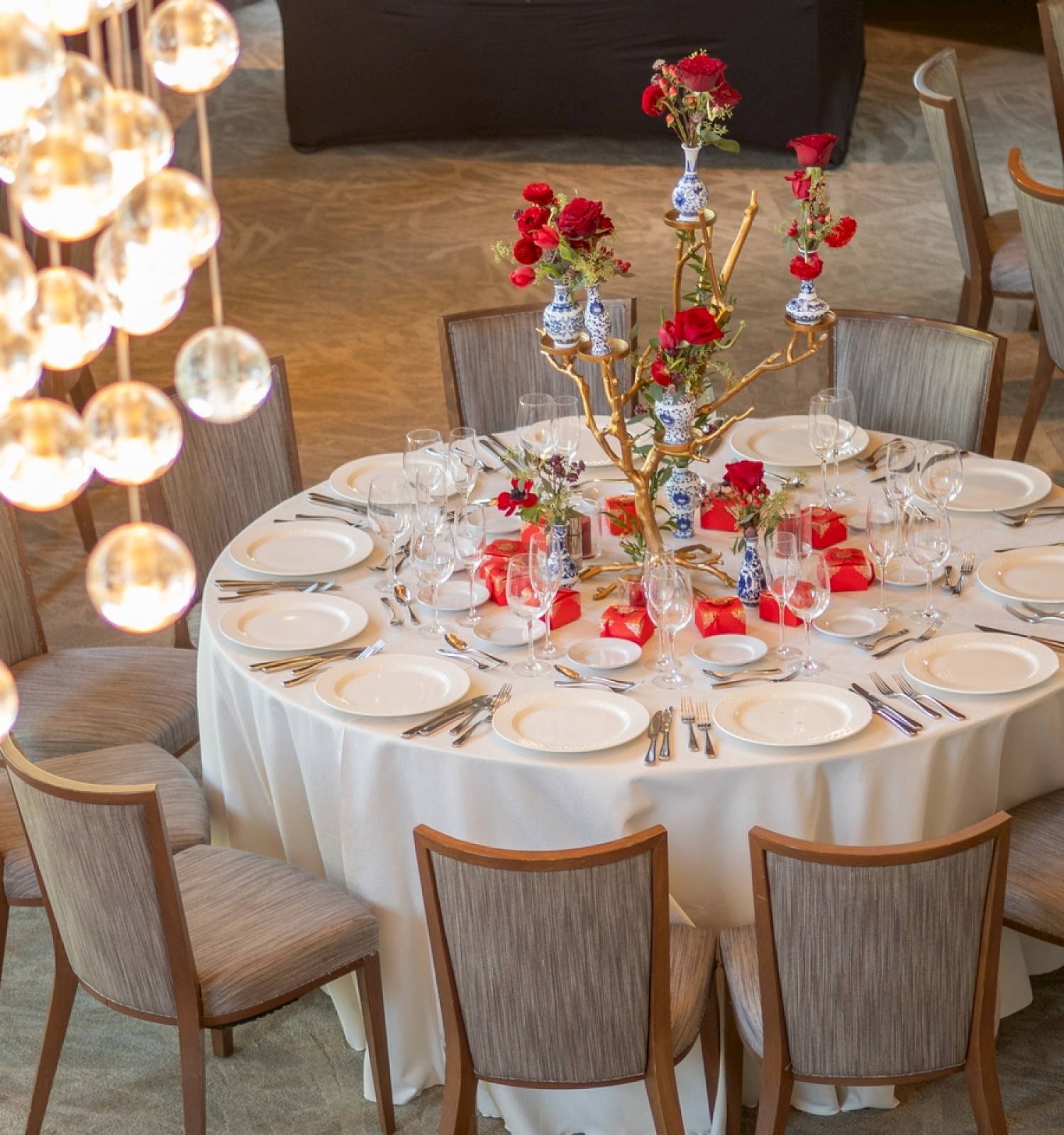 A round banquet table set with white linens, elegant place settings, tall floral centerpieces, and warm ambient lighting, ready for a formal event.