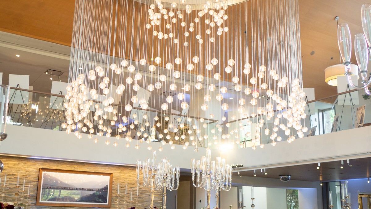 Elegant event hall with a large, modern chandelier and round tables set for a formal gathering or celebration.