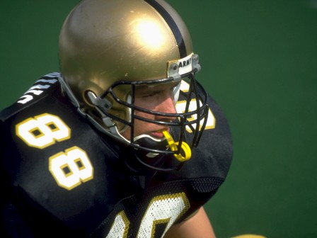 A football player is wearing a black jersey with the number 88 and a gold helmet, preparing for a game.