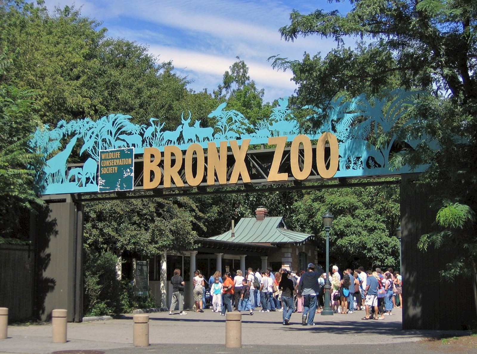 The image shows the entrance to the Bronx Zoo with people gathered underneath the sign.