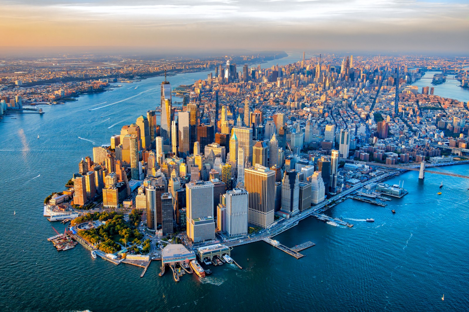Aerial view of a bustling cityscape with skyscrapers, surrounded by water, likely depicting a major metropolitan area at dusk.