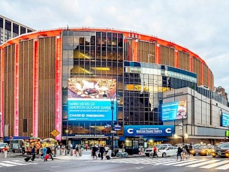 The image shows Madison Square Garden, a famous multi-purpose indoor arena in New York City, with bright lights and large billboards.
