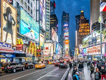 A bustling city scene with bright billboards, crowds, and traffic at night, likely depicting Times Square in New York City.