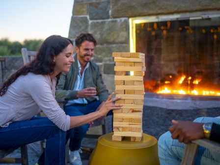 People are playing a wooden block tower game near a fireplace.