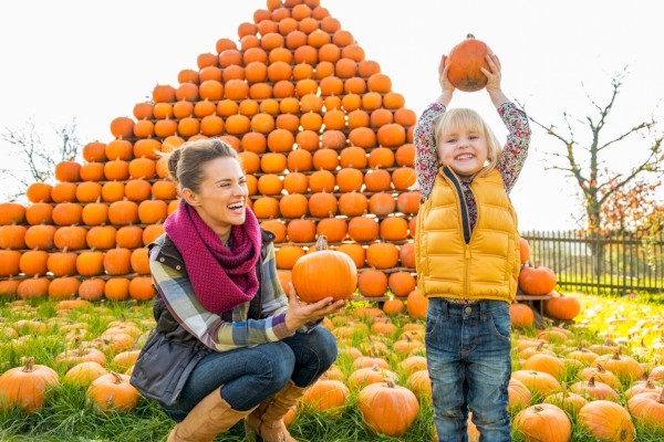 Young girl holding pumpkin overhead smiling with excitement, mom and daughter enjoying Halloween activities at Windrose on Hudson.