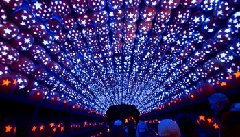 A tunnel illuminated with blue lights and star-patterned lanterns overhead, with people walking through.
