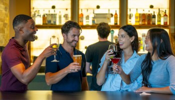 A group of four people enjoying drinks and chatting at a bar, with a bartender in the background.
