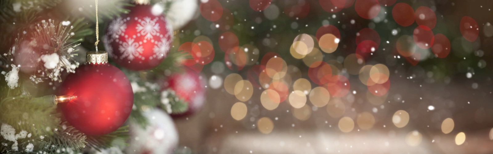 A Christmas tree with red ornaments is adorned with snow, accompanied by a blurred background with festive lights and a bokeh effect.