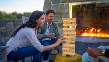 A group of people is playing a block-stacking game near a cozy outdoor fireplace, enjoying a relaxing and fun time together.