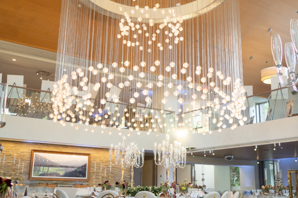 A luxurious banquet hall decorated with elegant tables, floral centerpieces, and a stunning modern chandelier overhead.
