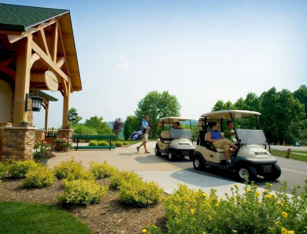 The image shows a golf course entrance with a building, plants, and two golf carts. A person is walking with golf clubs towards the building.