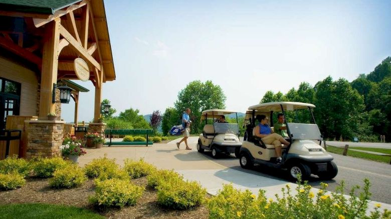 The image shows a golf course setting with people near a clubhouse and two golf carts, surrounded by greenery and landscaped shrubs.